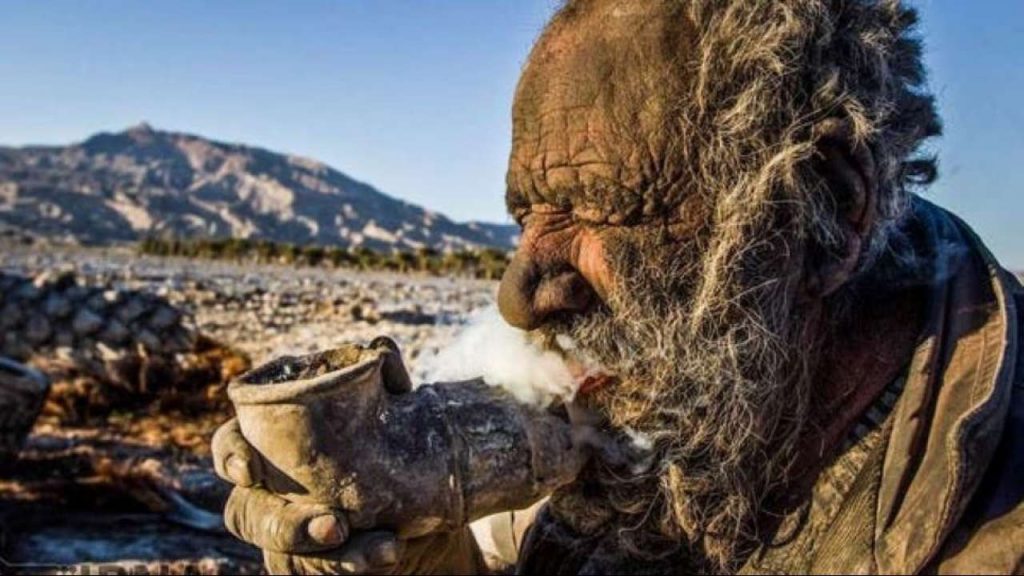 Amu Haji is doing his favorite thing — smoking dry manure through a metal pipe. Photo: IRNA