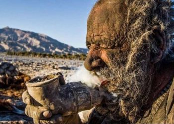 Amu Haji is doing his favorite thing — smoking dry manure through a metal pipe. Photo: IRNA